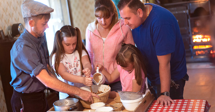 family learning how to cook at Beamish Museum 1940s farm house with roaring fire in background.